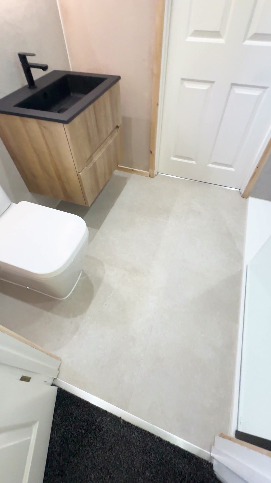 Minimalist bathroom with a timber vanity, dark basin and wall-hung toilet.