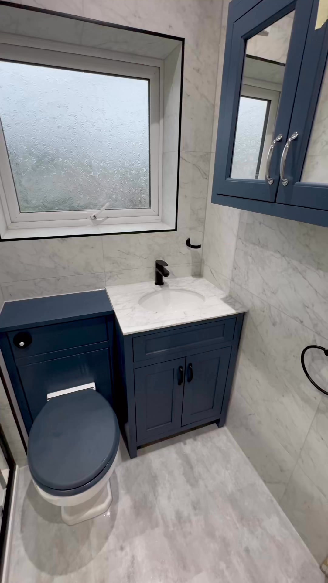 Compact tiled bathroom with a dark-blue vanity, white basin, toilet and window.