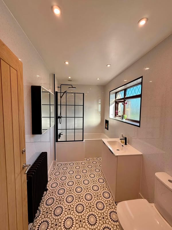 Bright family bathroom with pale wall panels, patterned flooring, a black-framed bath screen and vanity unit.