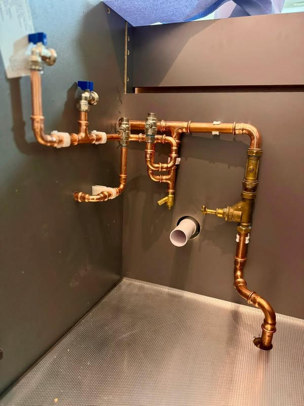 Copper pipework with valves and a waste connection, visible before the bathroom fittings are installed.